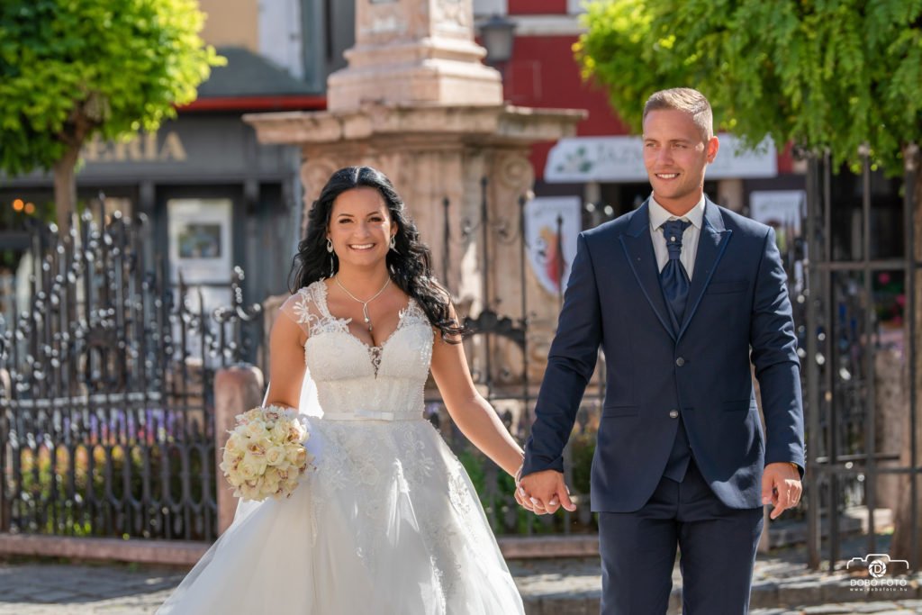 A boldog pár esküvői sétája Hajdúböszörmény romantikus utcáin, ahol a menyasszony gyönyörű csipkés ruhájában és a vőlegény elegáns öltönyében sugárzó boldogságot árasztanak. Az esküvői fotózás emlékezetes pillanatai egyedi helyszíneken kerültek megörökítésre.