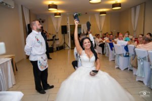 Az ifjú pár egy klasszikus esküvői cipős játék közben, ahol a nevetés és jókedv uralja a hangulatot. Az esküvői fotós megörökítette ezt az emlékezetes pillanatot, amely a vendégek mosolyát és a pár örömét is megmutatja.