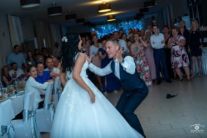 Az ifjú pár fergeteges esküvői tánca Hajdúböszörményben, ahol a mosolygó vendégek tapsolva élvezik az esküvői mulatság vidám pillanatait. Az esküvői fotózás során készült kép tökéletesen visszaadja az esküvő felejthetetlen hangulatát és boldog pillanatait.