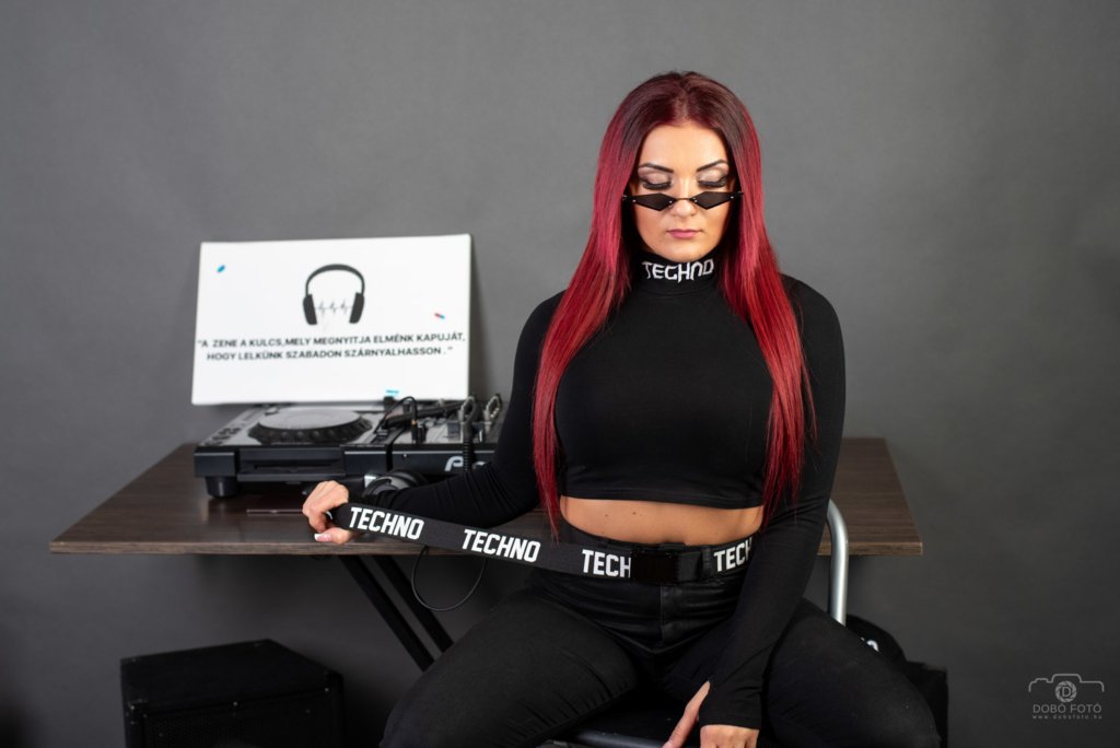 echno stílusú stúdiófotózás fekete outfitben, DJ eszközökkel és inspiráló idézettel. A profi fotózás során kreatív kiegészítők és modern dizájn elemek emelik a hangulatot.