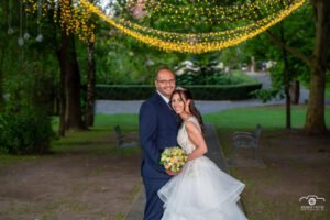 Esküvői portré Park Hill romantikus környezetében, a háttérben gyönyörű fényfüzér díszítéssel, boldog pár ünnepli szerelmét.