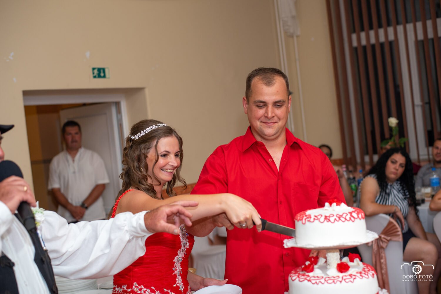 Esküvői tortavágás boldog pillanata – menyecskeruhás menyasszony és vőlegény, esküvői vacsora, torta, esküvői fotózás, vidám hangulat.