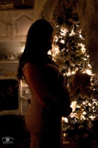 Karácsonyi hangulatú várandós fotózás gyengéd fényekkel, a kismama és az ünnepi díszek harmóniájában, a családi emlékek megörökítése.