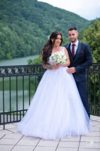 Esküvői pár a tó felett, természetes környezetben. Menyasszony fehér, hercegnős ruhában, vőlegény sötétkék öltönyben. Profi esküvői fotózás, természetes fények, romantikus hangulat, professzionális esküvői fotós munka.