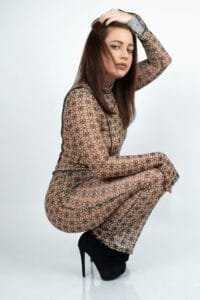 Egy nő portré fotózáson modern geometrikus mintájú testszínű outfitben, amely kiemeli az eleganciát és az egyedi stílust. A modell haját finoman igazítja, miközben fekete magas sarkú cipőjével és letisztult háttérrel harmóniát sugároz. A fotó Debrecenben készült professzionális portré fotózáson, mely az esztétikát és a kreativitást ötvözi.