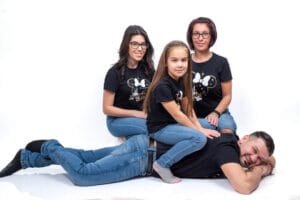 Debreceni családi fotózás, ahol a család tagjai mosolyognak és játékos pózban helyezkednek el, fekete pólóban és farmerben, fehér stúdióháttér előtt.