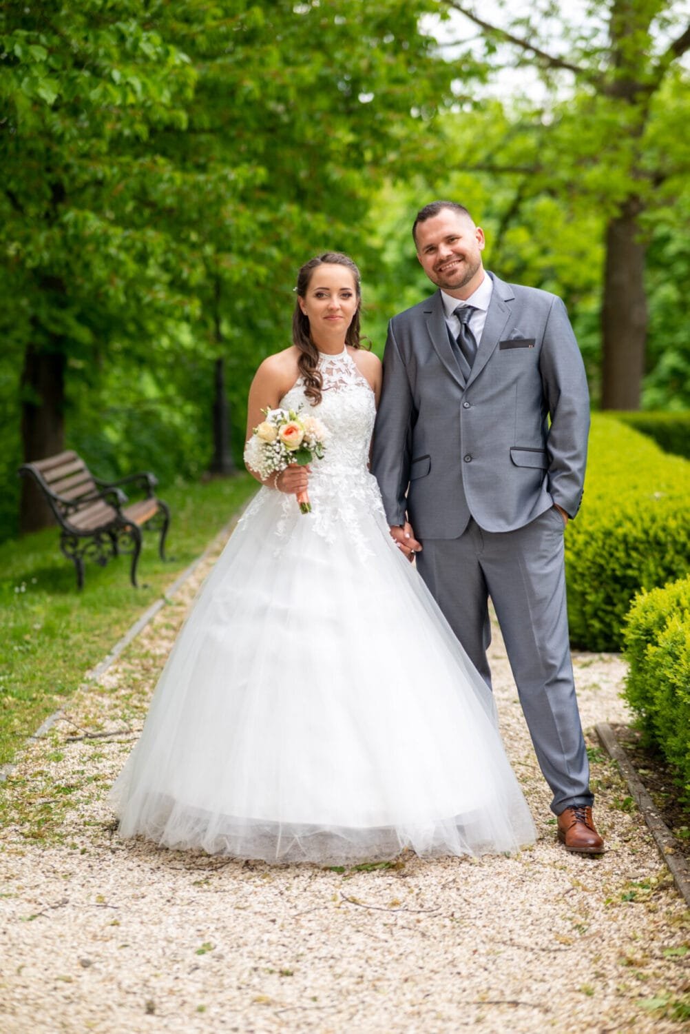 Ifjú pár elegáns esküvői ruhában, zöldellő természet és parkos környezet ölelésében, Lillafüreden készült esküvői fotón.