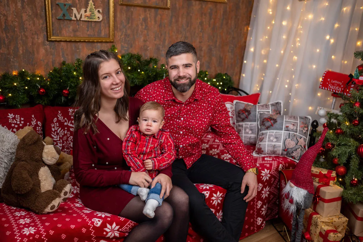 Egy boldog család ünnepi fotója, piros ruhákban, karácsonyi díszek között, Debrecenben készült karácsonyi fotózás során.