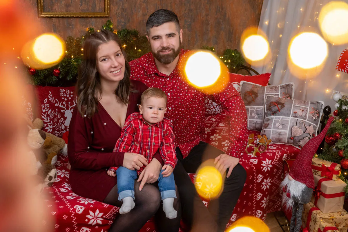 Egy fiatal család közös karácsonyi fotózáson, ünnepi díszletekkel, piros ruhákban, meghitt és örömteli hangulat Debrecenben.
