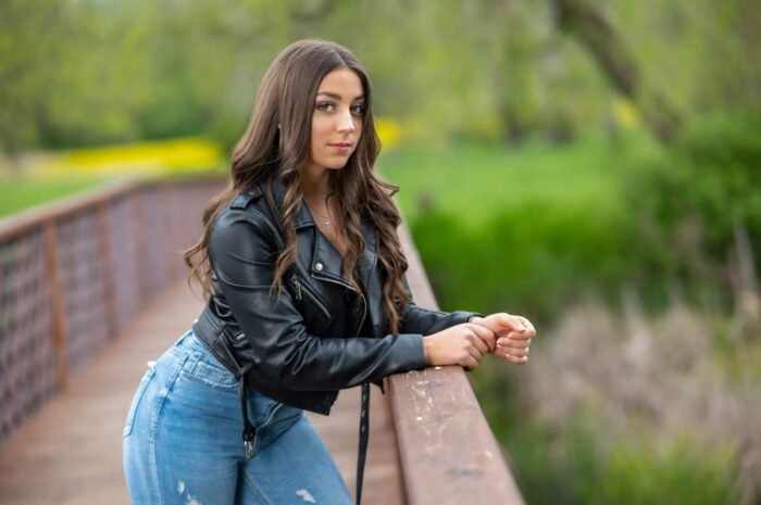 Fiatal nő fekete bőrdzsekiben és kék farmerben, a Vekeri-tónál lévő fahíd korlátjára támaszkodva, gyönyörű zöld és sárga természetes háttérrel, Debrecen közelében.