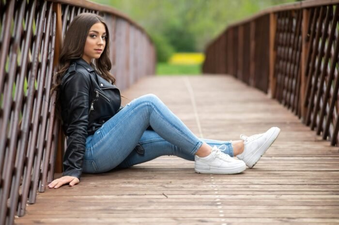 Fiatal nő fekete bőrdzsekiben és kék farmerben ül egy fa hídon, szabadtéri fotózás során, a Debrecen melletti Vekeri-tónál.