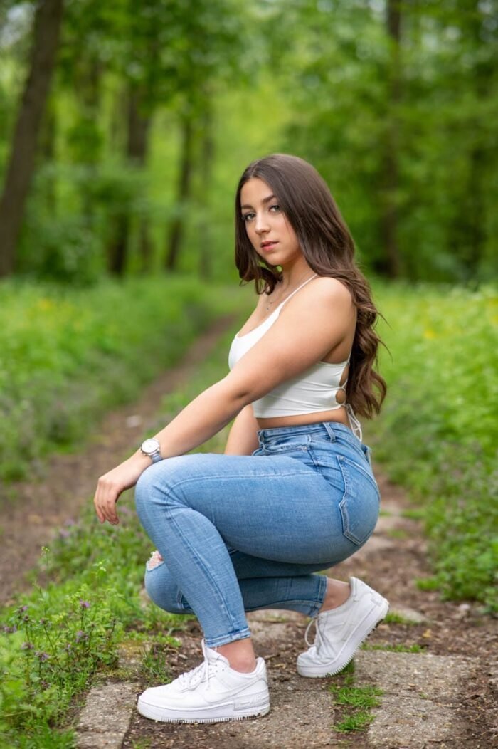 Fiatal nő fehér topban, farmernadrágban és sportcipőben, a Vekeri tó erdei ösvényén készült portréfotó.