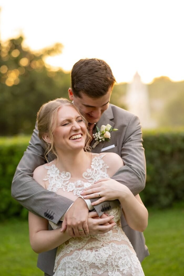 Debreceni esküvői fotós képe. Az ifjú pár nevetve öleli egymást egy romantikus, naplementés háttér előtt, a menyasszony csipkés ruhában, a vőlegény elegáns öltönyben.