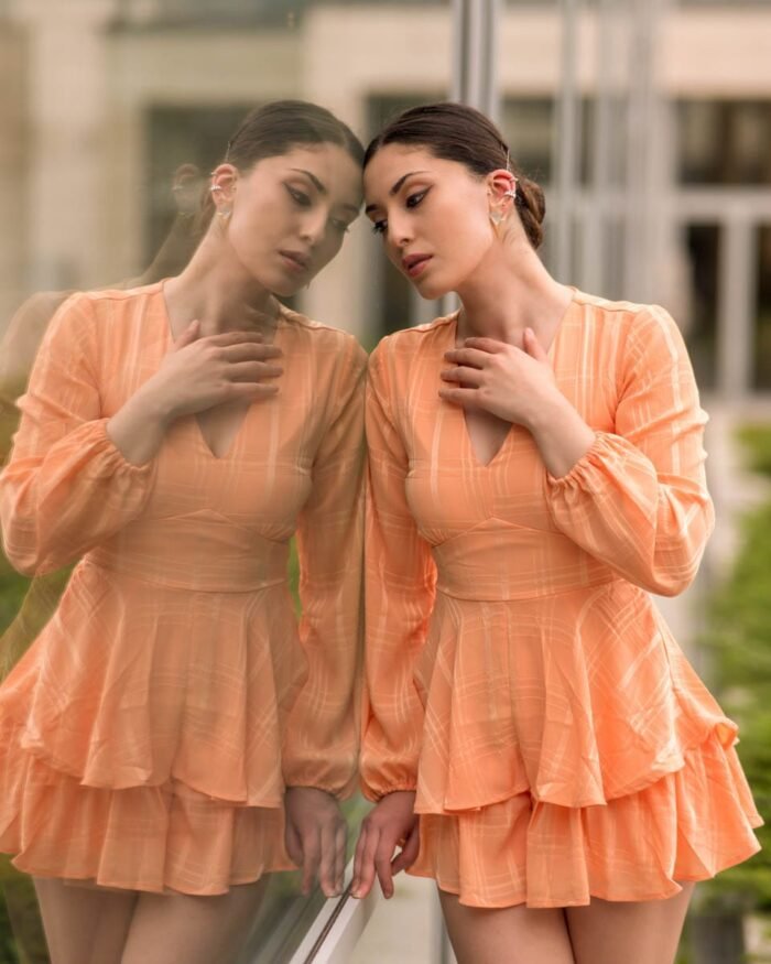 Fiatal nő narancssárga ruhában egy üvegfelület előtt, amely visszatükrözi alakját, Debrecenben készült portréfotó.