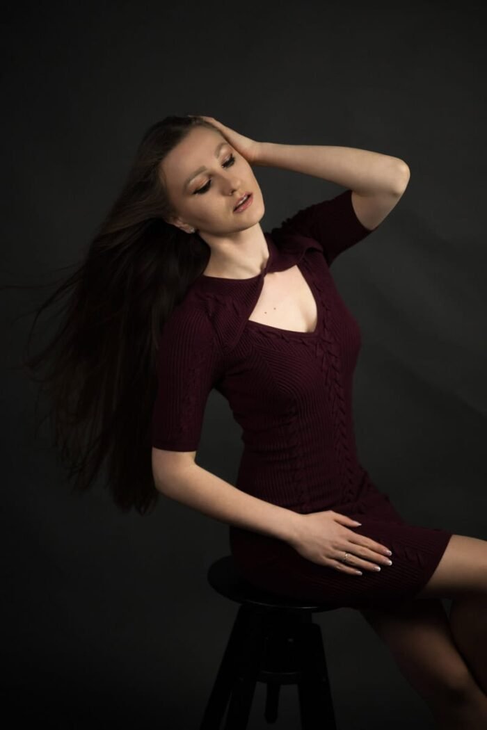 Egy elegáns portréfotó debreceni stúdióban, ahol egy hosszú, barna hajú nő bordó ruhában ül egy széken, háttérben sötét tónusú háttérrel.