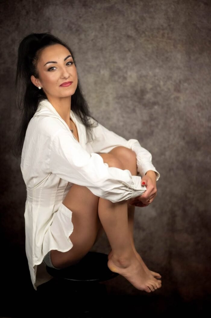 Debreceni stúdióban készült portré, elegáns nő fehér ingben, természetes pózban, szürke háttér előtt.