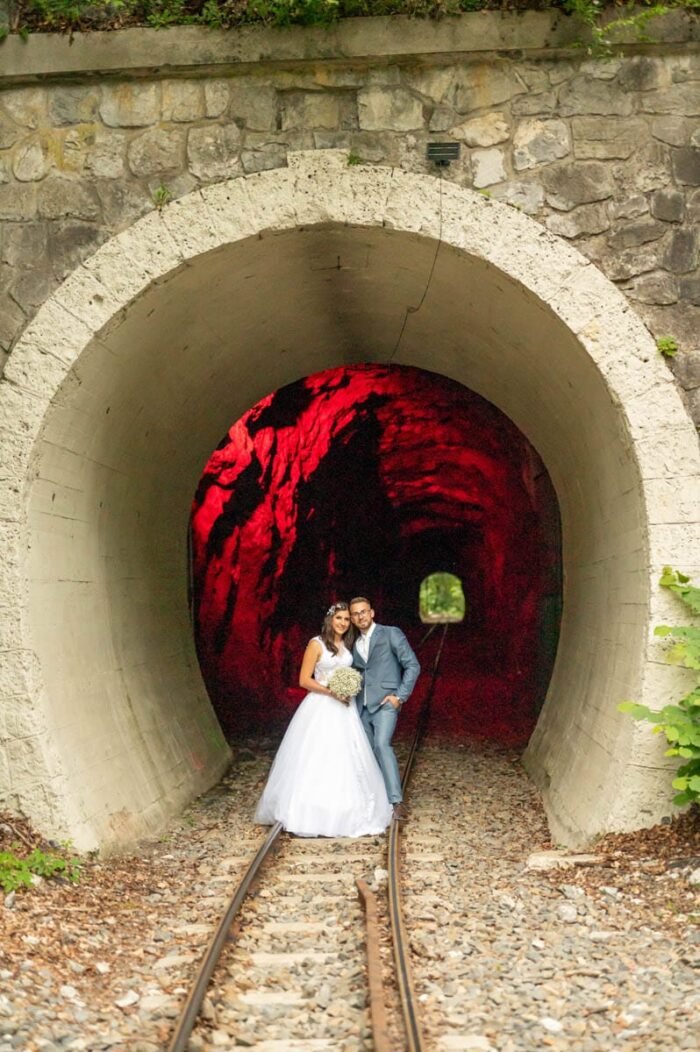 A fiatal pár egy vasúti alagút előtt áll, miközben a menyasszony esküvői ruhát visel, a vőlegény pedig elegáns öltönyt. Az alagút belső terét piros fények világítják meg, a sínek mentén állnak. A menyasszony a kezében tartja a virágcsokrot, miközben boldogan mosolyognak egymásra.