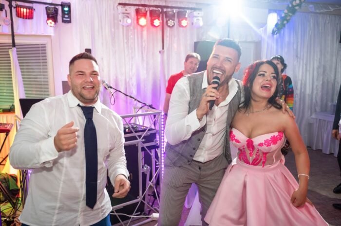 A hangulat a tetőfokára hág, miközben a násznép táncol és énekel a buli alatt. Jolly és a menyasszony élvezik a pillanatot, miközben a háttérben a vendégek táncolnak, egy színes fényekkel díszített helyszínen. A fények és a zene mindent beborítanak, és a vendégek szórakoznak az esküvői partijukon.