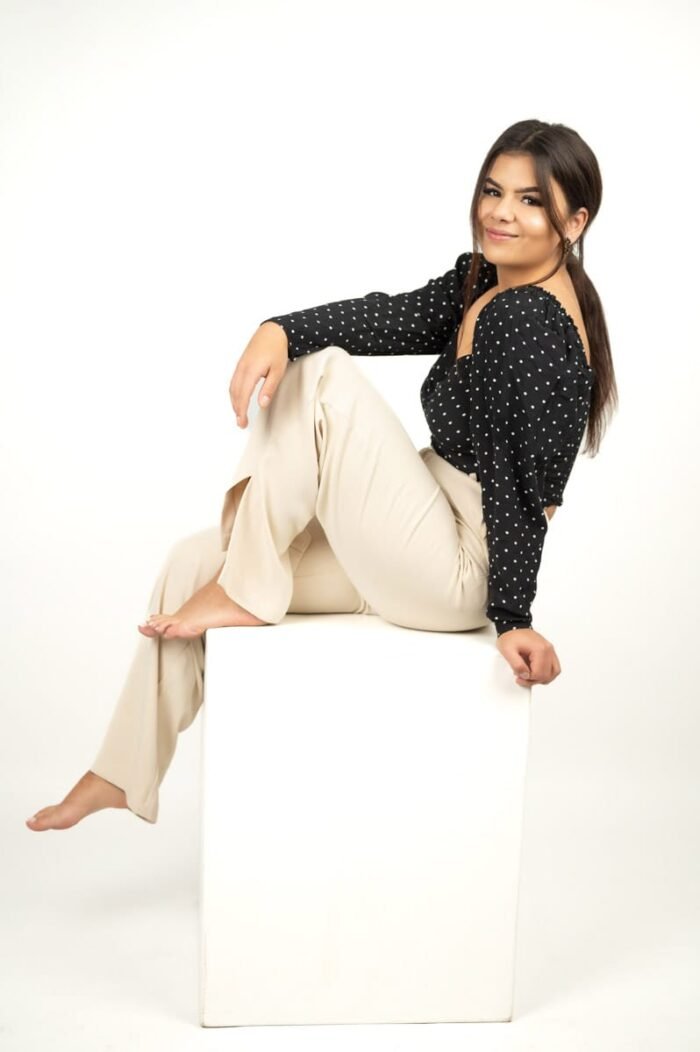 Fiatal nő fekete pöttyös felsőben és bézs nadrágban ül egy fehér kocka elemre támaszkodva egy letisztult stúdiókörnyezetben Debrecenben.