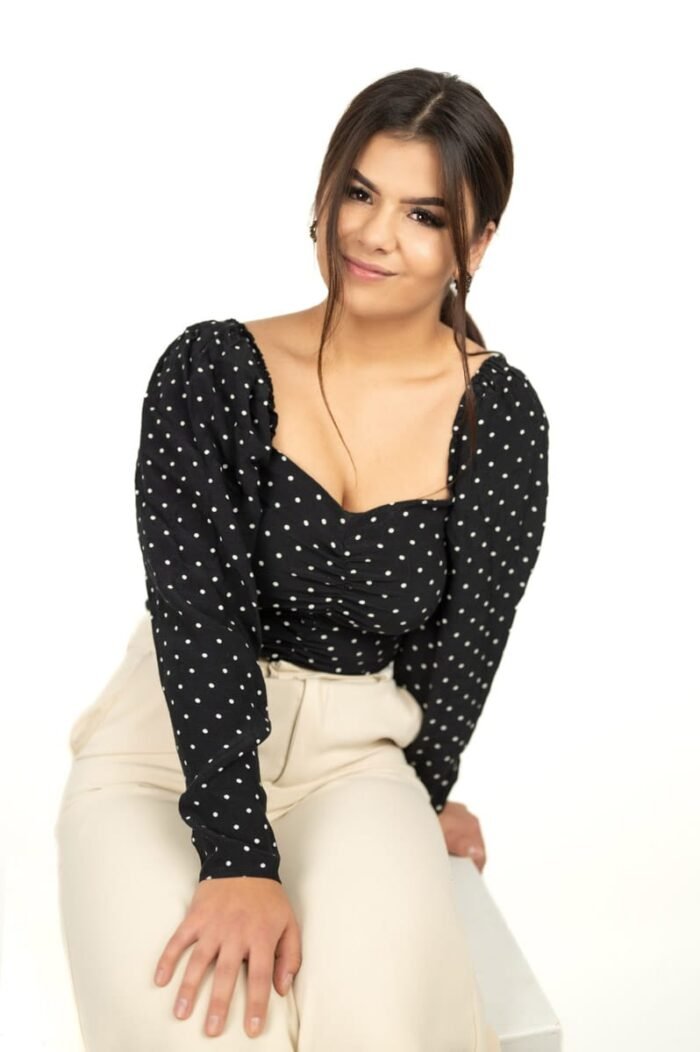 Fiatal nő fekete pöttyös felsőben és bézs nadrágban, természetes mosollyal egy stúdiófotón Debrecenben.