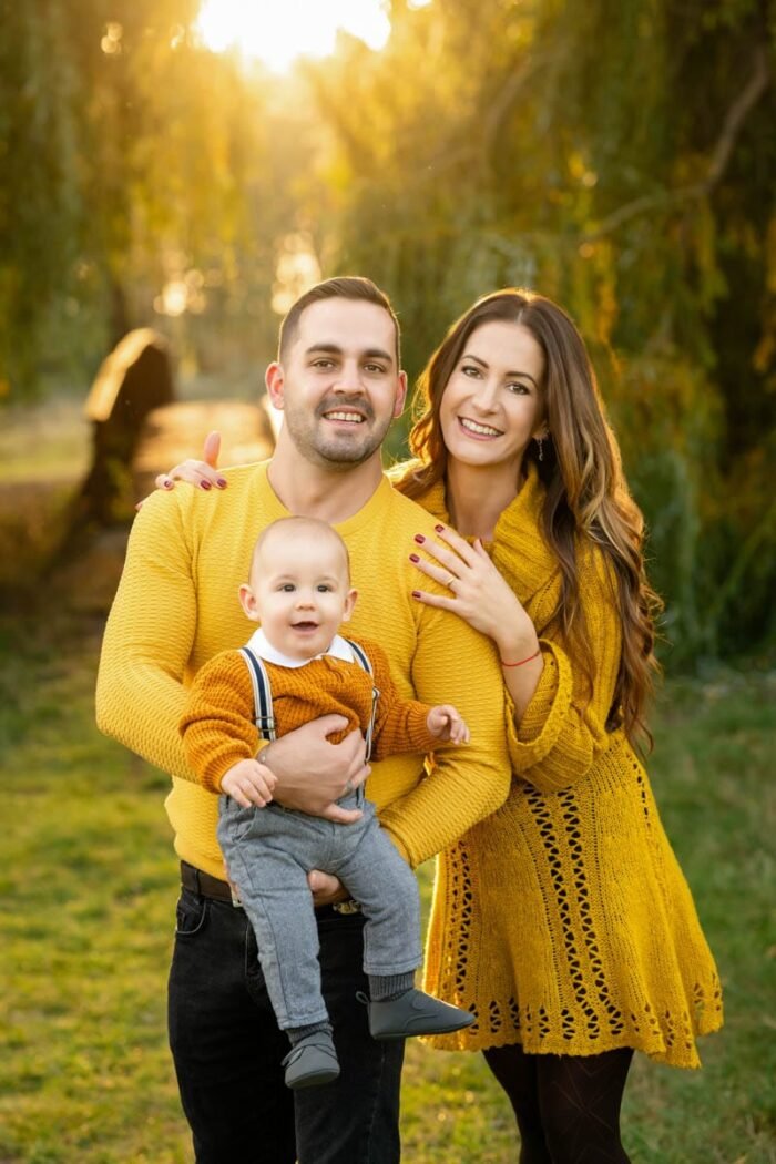 Egy boldog család, mindegyikük sárga pulóverekben, a szabadban, napsütéses időben. Az apa kezében tartja kisfiát, aki mosolyogva néz a fényképezőgépre. Az anya mellette áll, kezét az apára helyezve, mindketten boldogan mosolyognak. A háttérben a természet, zöld fák és napfényes táj látható.