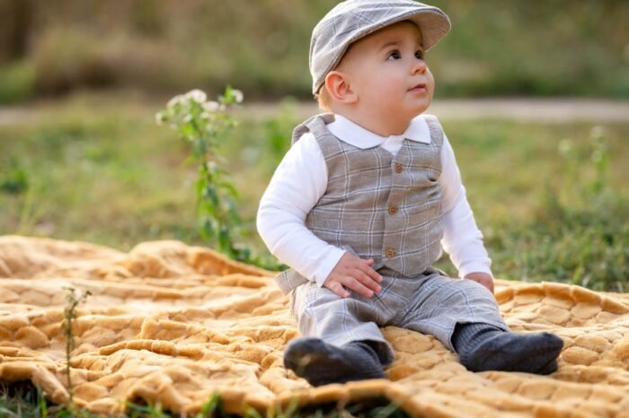 Szabadtéri gyermek fotózás Debrecenben - Egy kisfiú kényelmesen ül egy sárga pléden a szabadban, miközben elegáns öltönyben és sapkában néz fel a távolba.