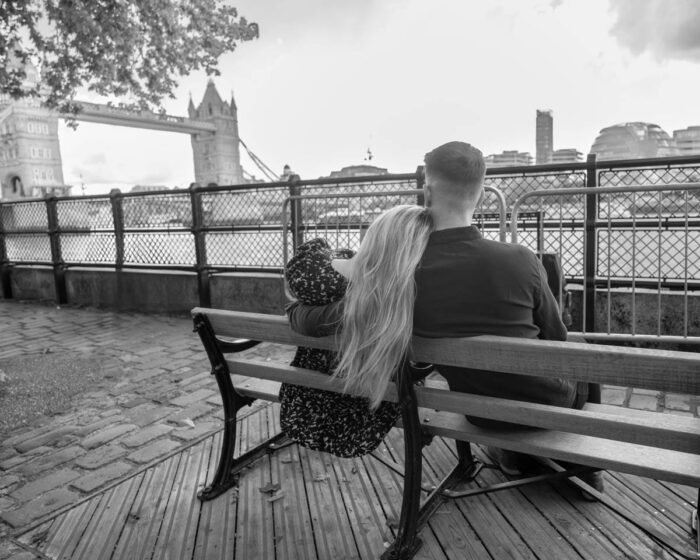 Egy jegyespár egy padon ülve, egymáshoz bújva figyeli a Tower Bridge-t és a Temze folyót Londonban. A fekete-fehér kép meghitt és romantikus hangulatot áraszt.