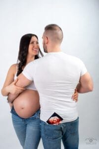Kismama fotós Debrecenben -Várandós pár ultrahanggal: kismama fehér topban és farmerben mosolyog, párja fehér pólóban, farmerja zsebében ultrahang kép.Műtermi fotózás.