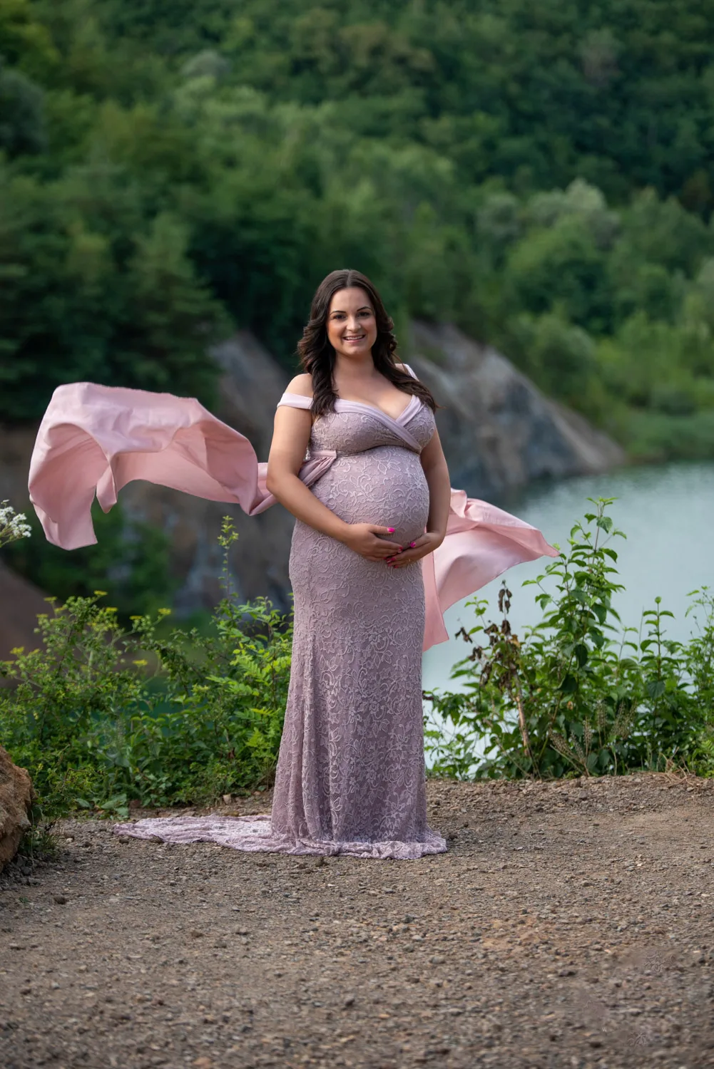 Kismama fotózás Debrecenben - Elegáns kismama fotózás tóparti háttérrel, várandós anyuka lila csipkeruhában, lobogó fátyollal. Természetes szépség és varázslatos pillanatok a szabadban.