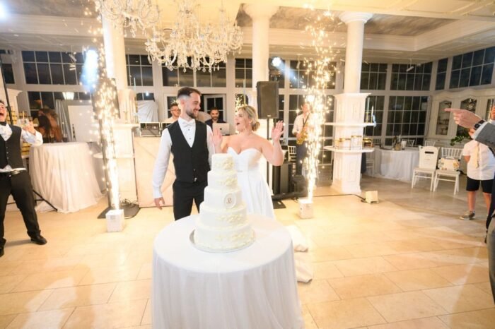 A menyasszonyi torta előtt áll a pár, boldogan mosolyognak, miközben készülnek felvágni az esküvői tortát, amely a nap egyik legkülönlegesebb pillanata.