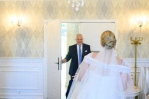 A menyasszony és édesapja meghitt pillanatban osztoznak, amikor az apa először látja lányát menyasszonyi ruhában, érzelmekkel teli mosollyal és könnyekkel a szemében.
