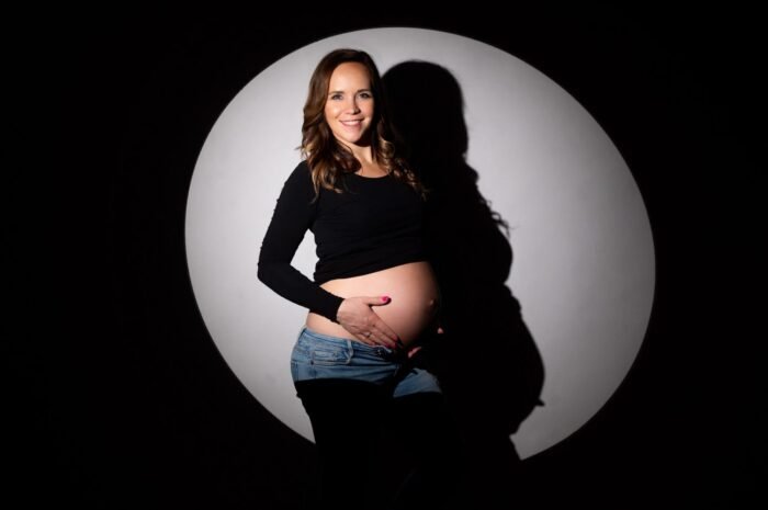 Kismama fotózás egyedi környezeti megvilágítással, várandós anyuka mosolyogva a kamera előtt.