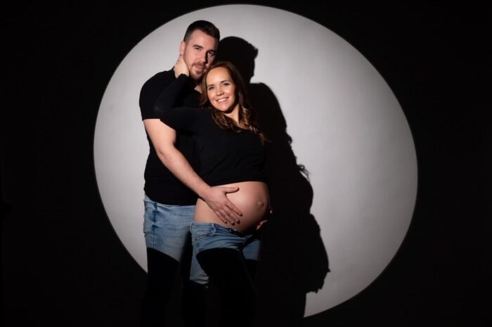 Kismama fotózás Debrecenben, pár meghitt pillanata egyedi megvilágítással, fekete háttér előtt.