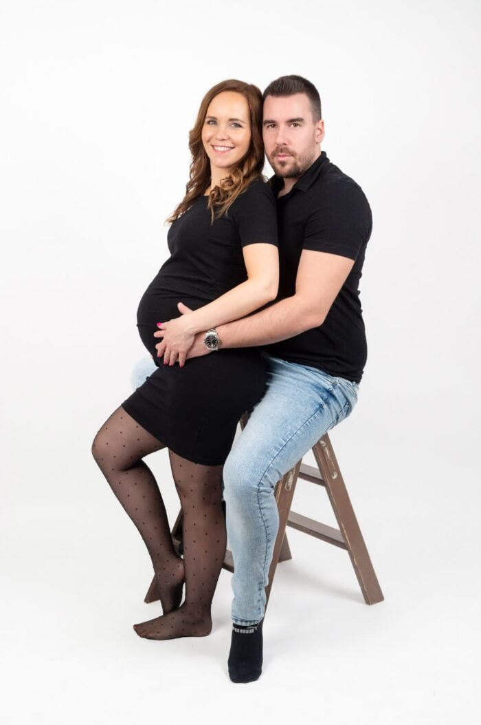 Kismama fotózás Debrecenben. Pocakos fotózás, boldog pár együtt, a kismama fekete ruhában, párja farmerben, fehér háttérrel és természetes hangulatban.