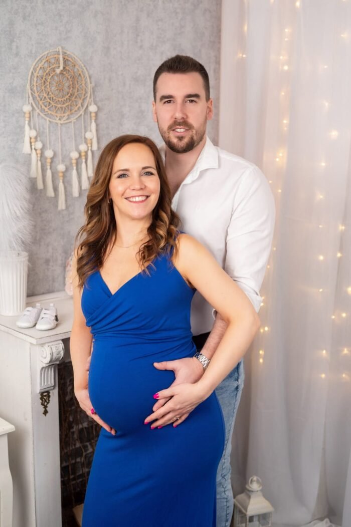 Pocak fotózás Debrecenben, kismama kék ruhában mosolyog, párja mellette áll, romantikus stúdió dekorációval a háttérben.