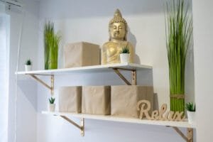 Egy kozmetikai szalon polca Buddha szoborral, növényekkel és „Relax” felirattal, amelyek a harmóniát és nyugalmat hangsúlyozzák a szalonban.