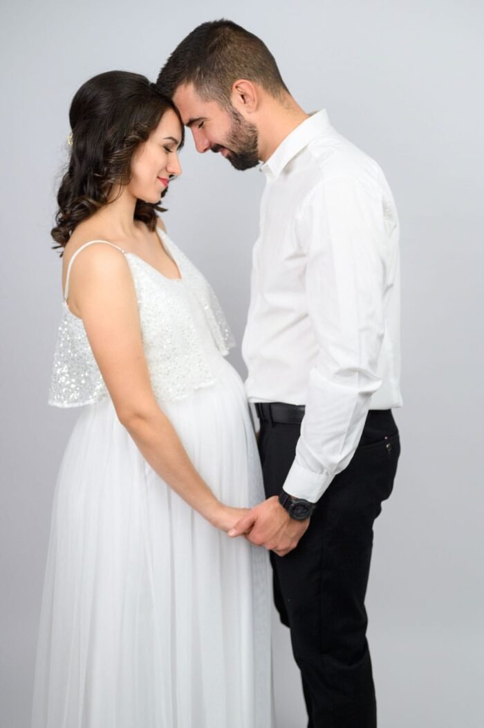 Egy fiatal pár gyengéden egymás homlokát érintve áll egymással szemben, kezük összekulcsolva. A kismama elegáns fehér ruhája és a pár szeretetteljes testbeszéde a családjukra váró boldog jövőt sugallja.