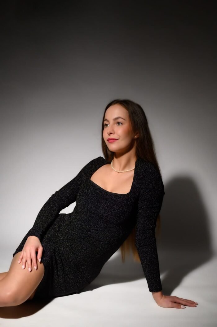 Portré fotózás Debrecen - Egy fiatal nő elegáns, csillogó fekete ruhában, gyöngysorral pózol árnyékos megvilágításban egy stúdióban.