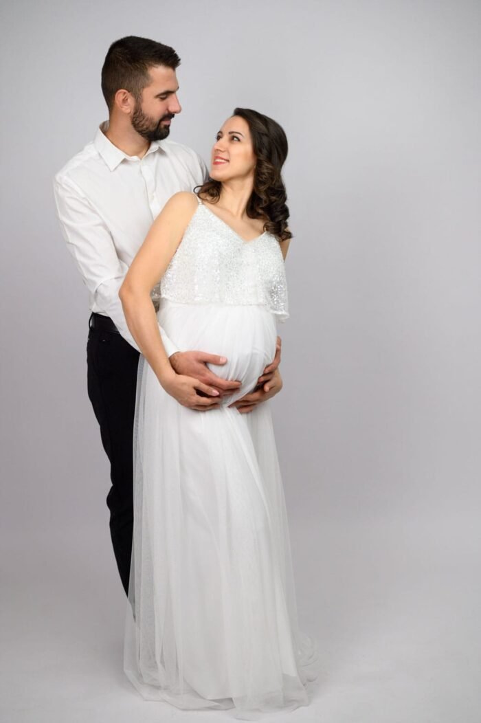 Debreceni ksimama fotós képe. A boldog pár egymásra nézve mosolyog, miközben a férfi gyengéden átöleli a kismama pocakját. A pillanat tele van szeretettel és az új élet érkezésének örömével.