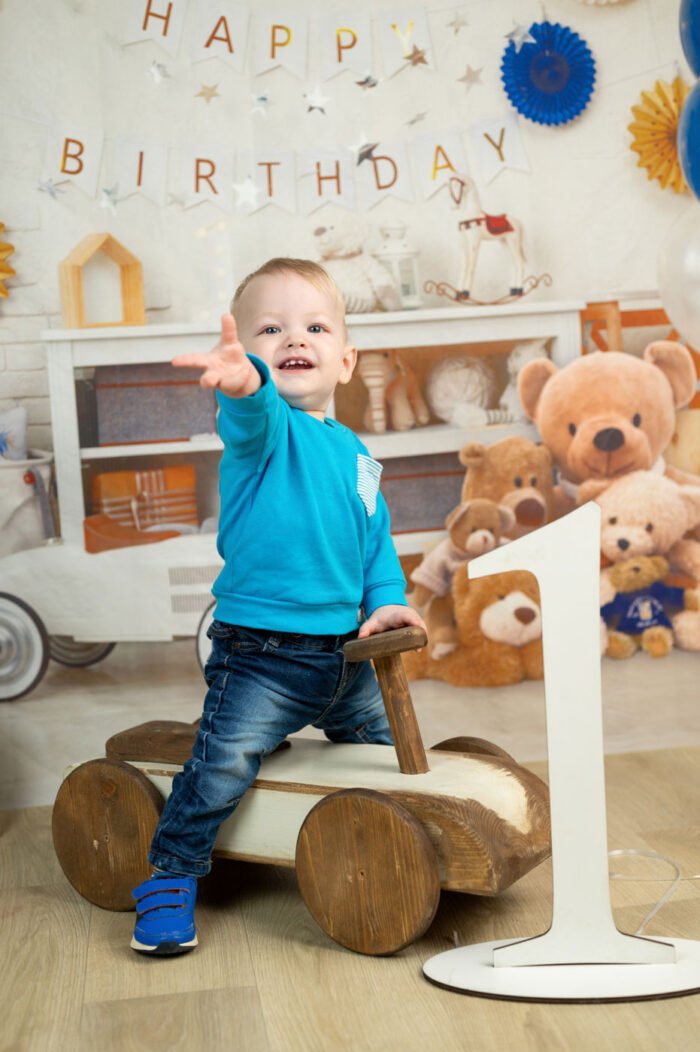 Kisfiú kinyújtott kézzel játszik, miközben szülinapi dekorációk és egy nagy egyes szám szerepel a háttérben.