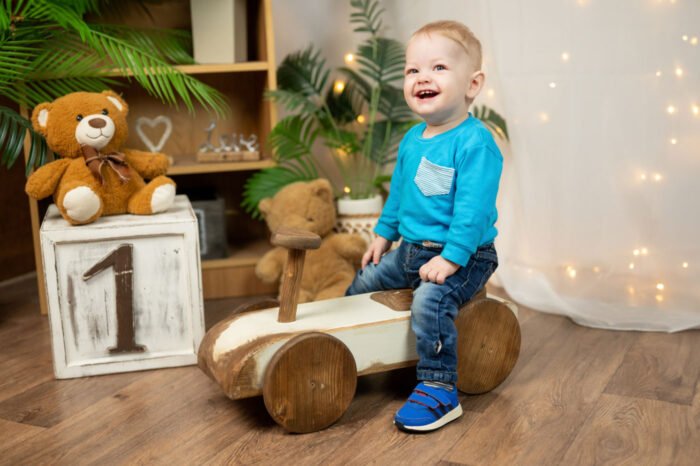 Születésnapi fotózás Debrecenben - Kisfiú vintage fa járművön játszik, mögötte ünnepi fények és aranyos plüssállatok.