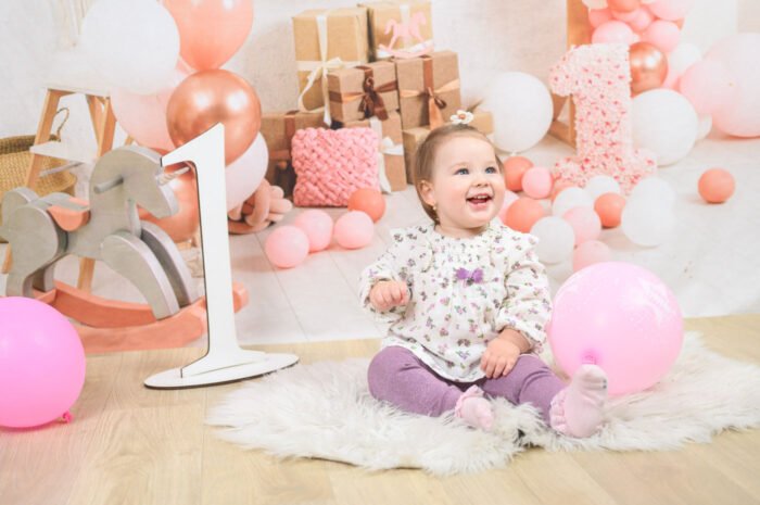Szülinapi fotózás Debrecen- Egyéves kislány szülinapi fotózása Debrecenben, rózsaszín és fehér dekorációval, lufikkal és ajándékokkal. Vidám babafotózás profi stúdiókörnyezetben.