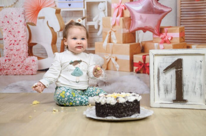 Fotós Debrecen – Egyéves kislány születésnapi fotózása tortamaszatolással. Babafotózás ünnepi dekorációval, rózsaszín lufikkal és ajándékdobozokkal profi stúdiókörnyezetben.