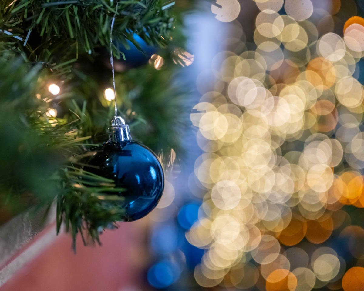 Kék karácsonyi gömb dísz a fán, háttérben arany bokeh fények.