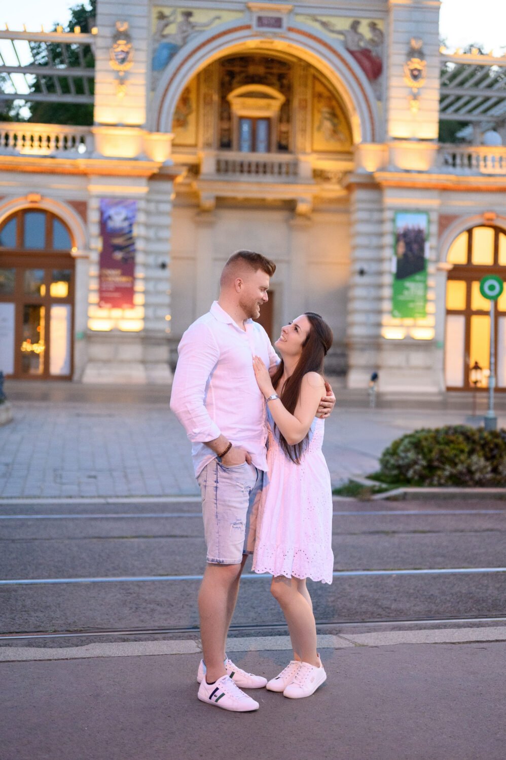 Jegyespár egymást átölelve áll a kivilágított, neoreneszánsz Várkert Bazár homlokzata előtt az esti fényben – budapesti jegyes fotózás.